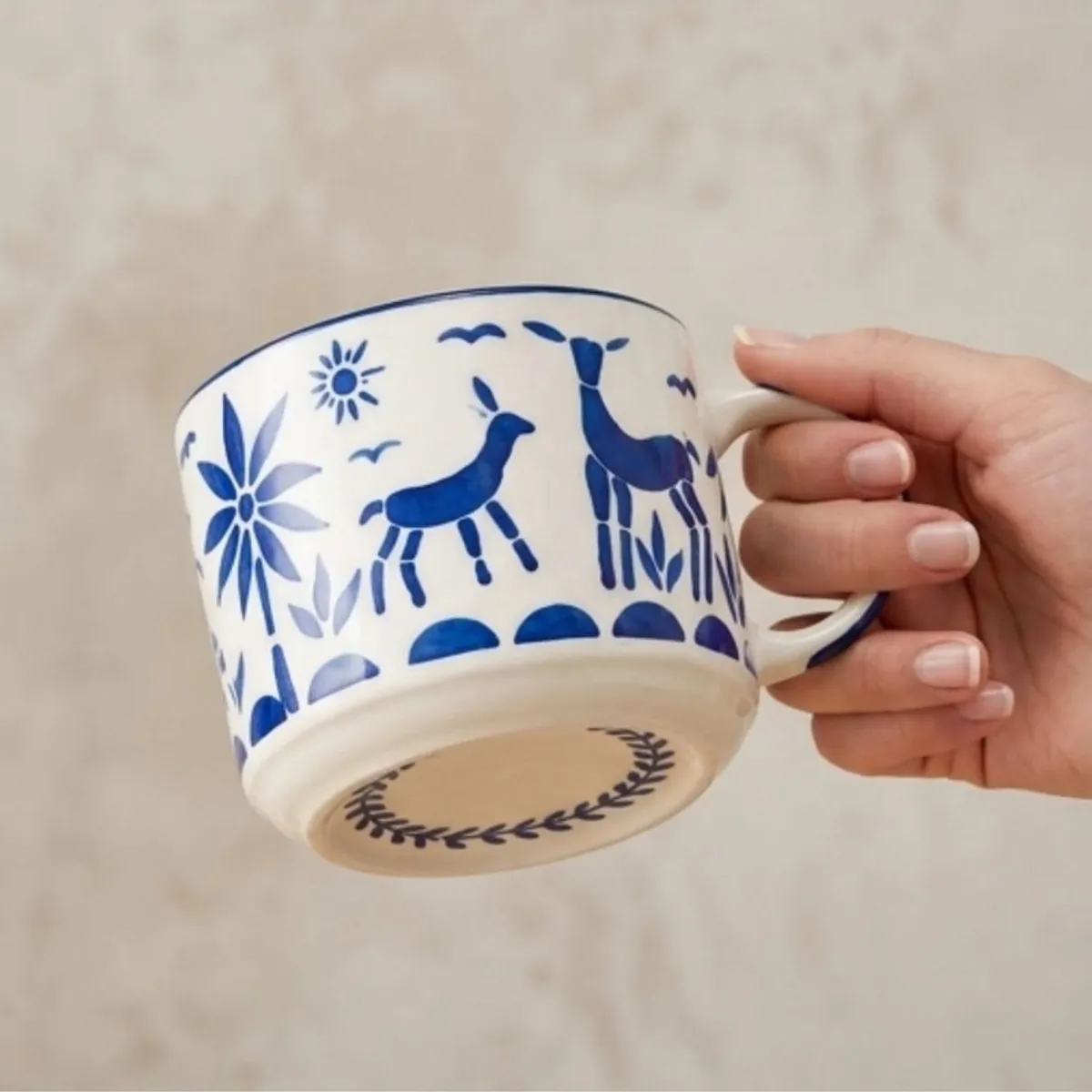 Hand holding a white ceramic cup decorated with blue reindeer and floral motifs.