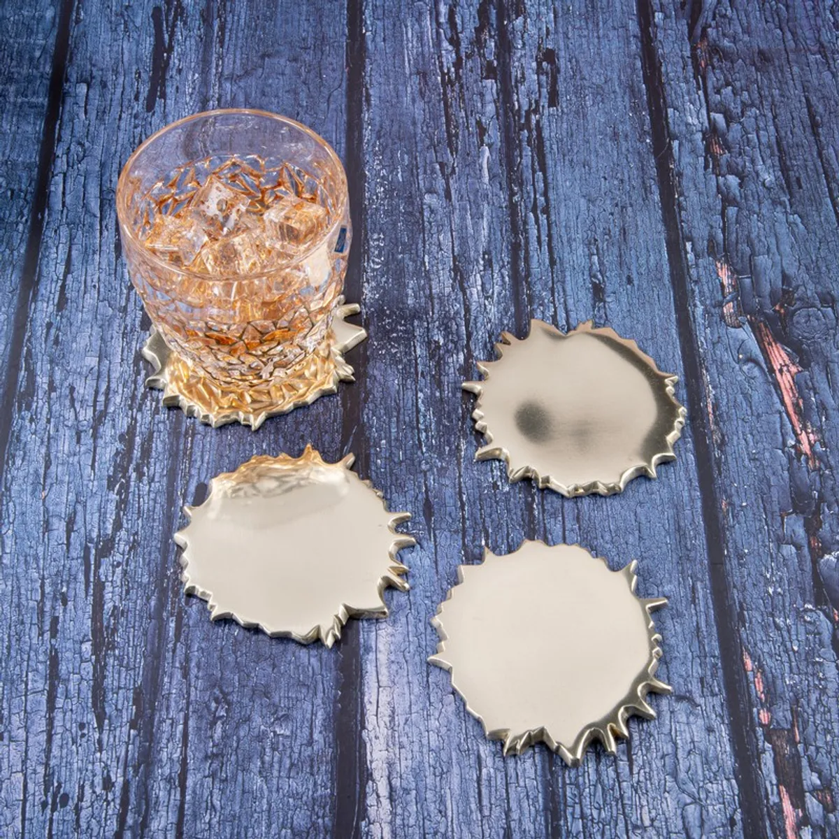 Gold spill-shaped coasters with a textured glass on a dark blue wooden surface