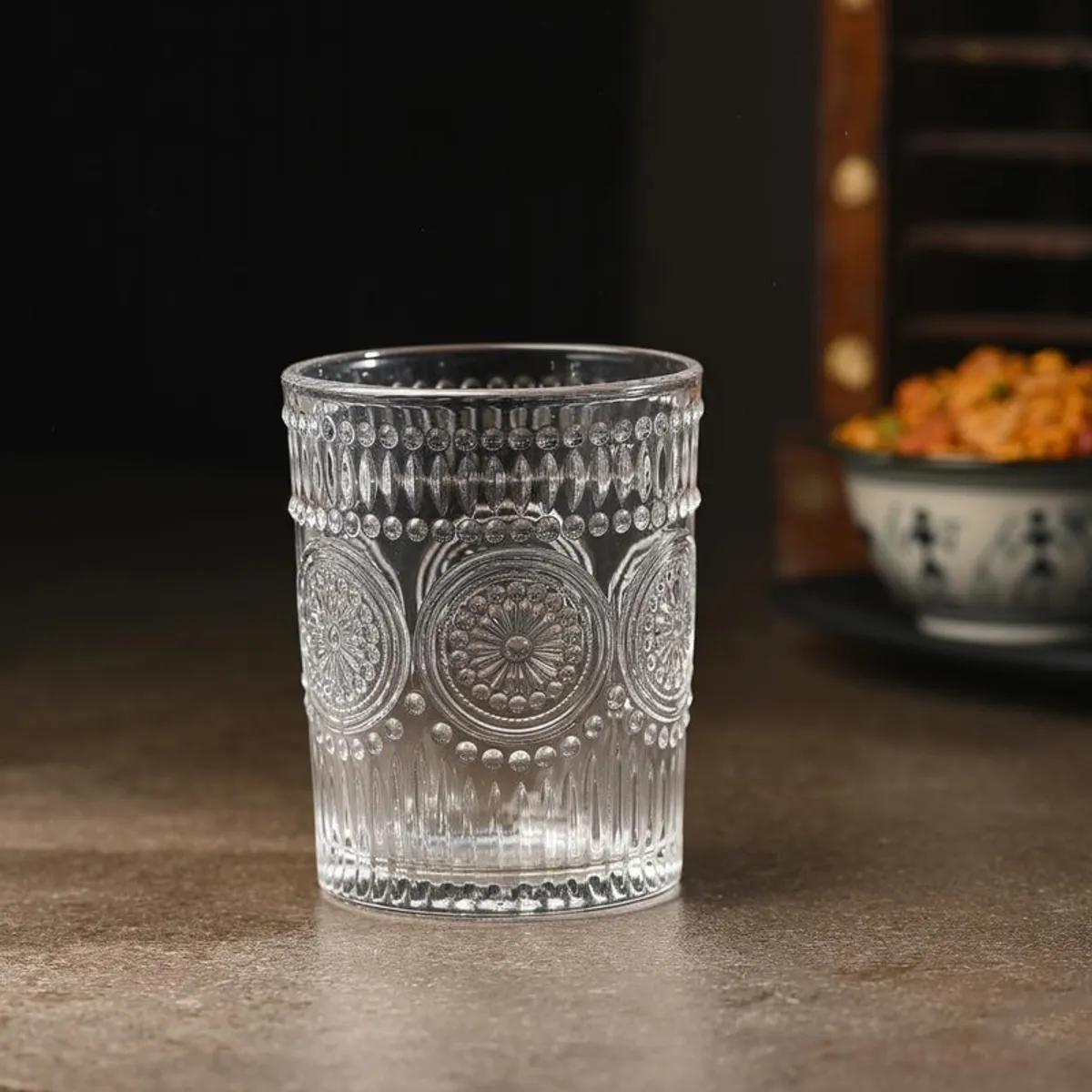 Single clear whiskey glass with ornate circular textured detailing on a dark table