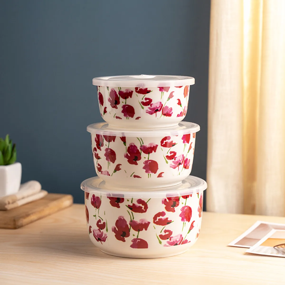 Three stacked pink floral containers with transparent lids on a wooden table