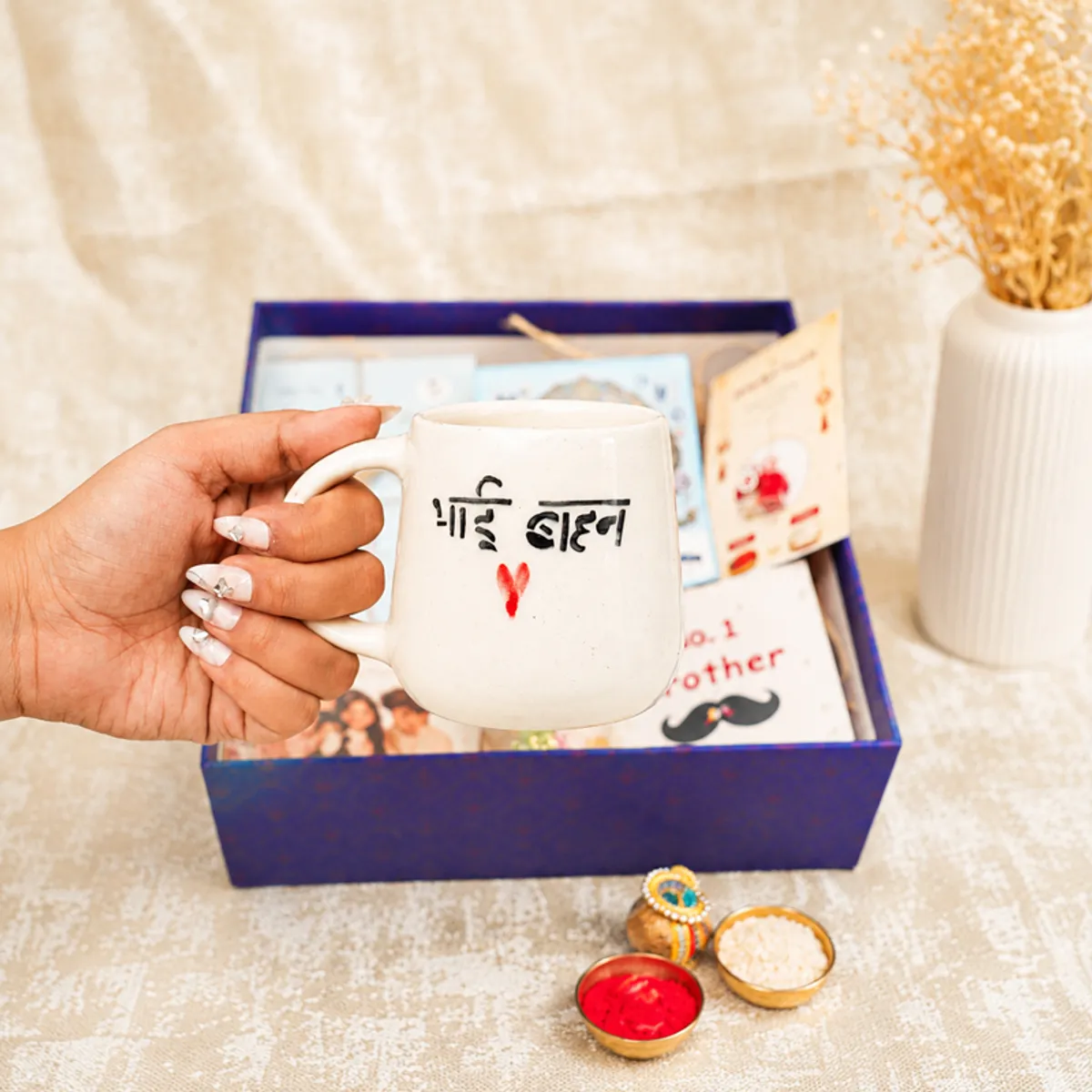 Hand holding the Bhai Behan ceramic mug above the open Raksha Bandhan gift box.