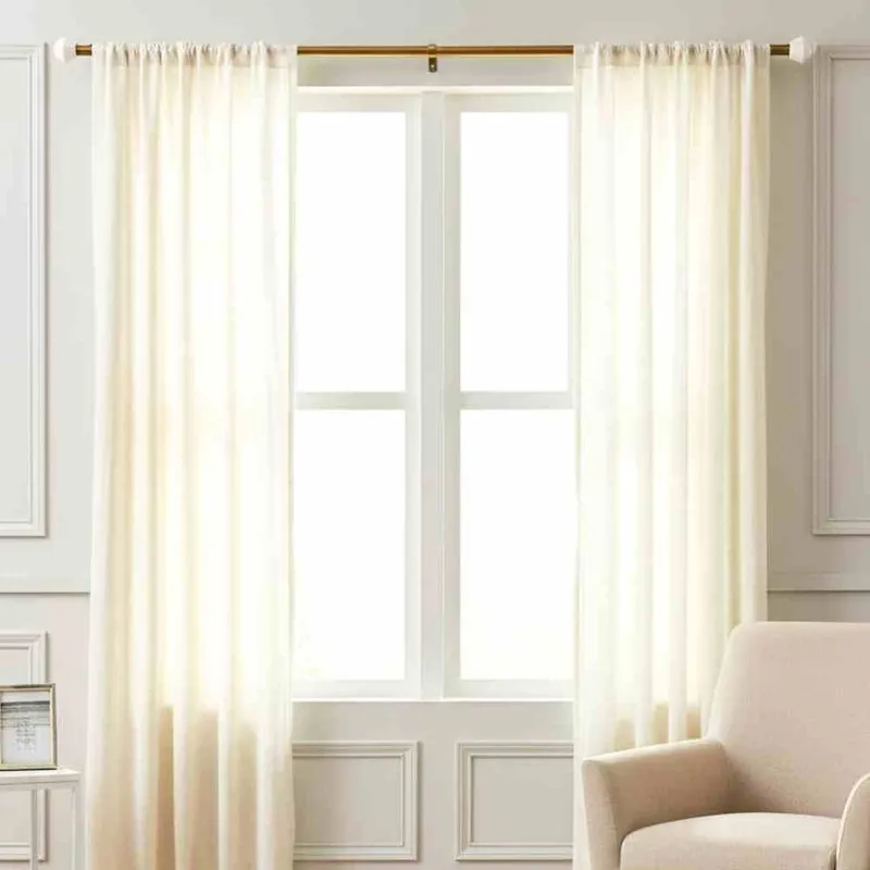 Gold curtain rod with white finials styled over a bright window with curtains