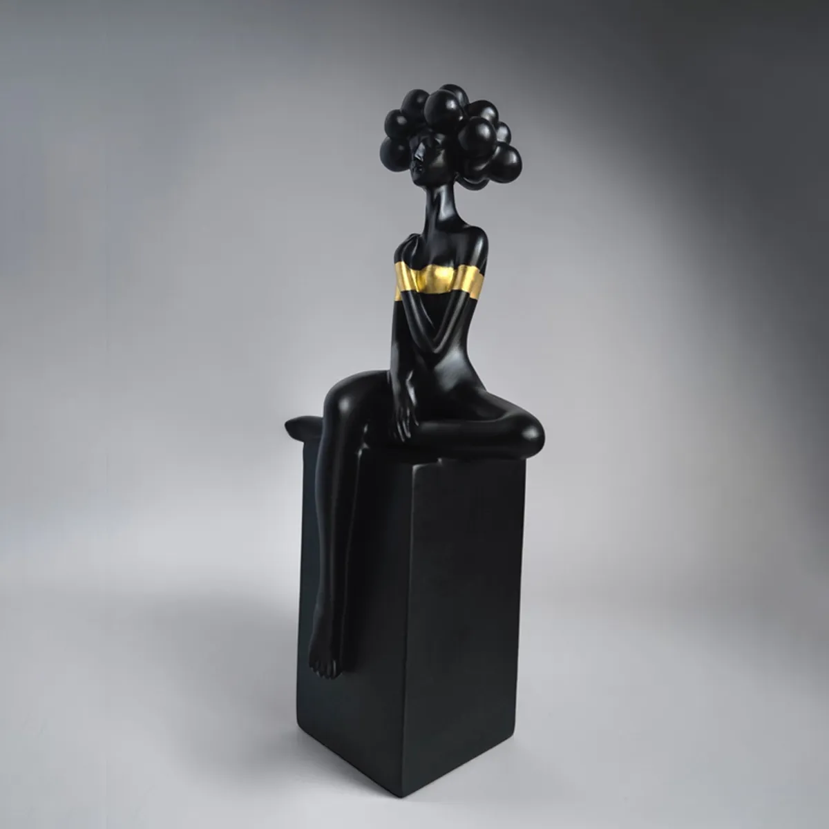 Black and gold seated lady sculpture photographed against a dark grey backdrop