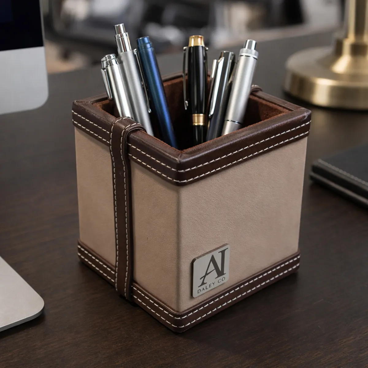 Grey and brown vegan leather pen stand holding assorted pens beside a laptop