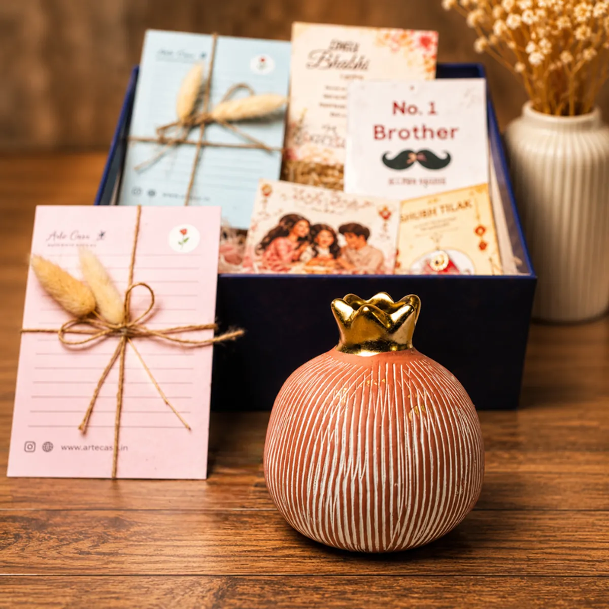 Pomegranate vase placed in front of the open Rakhi gift box with cards