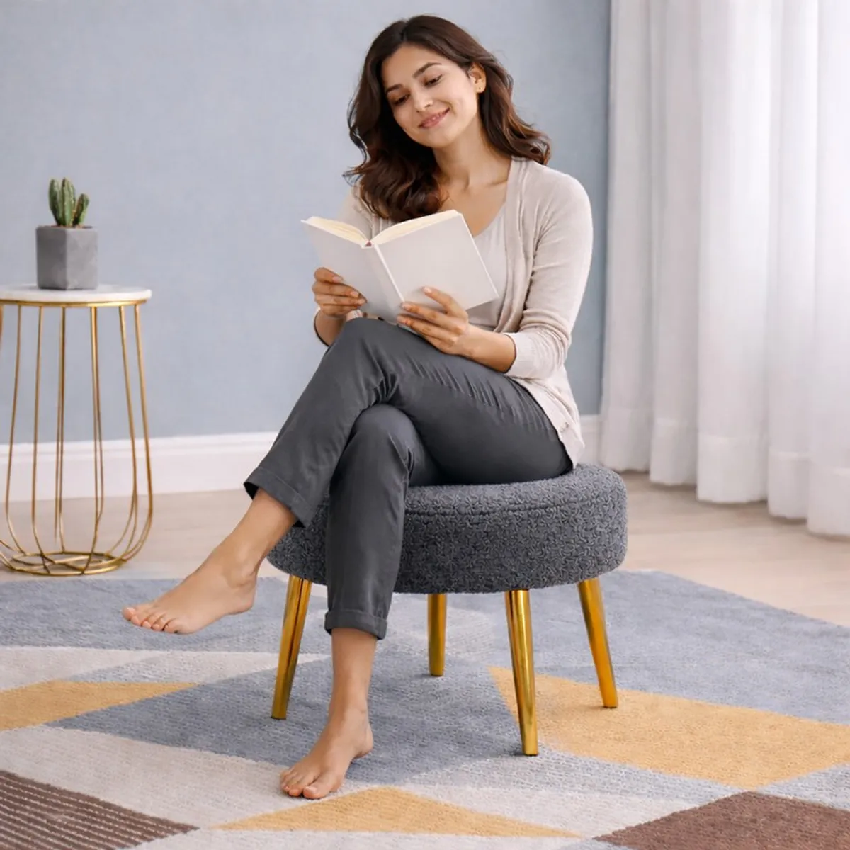 Person seated on a dark grey round bouclé stool with gold-finished legs