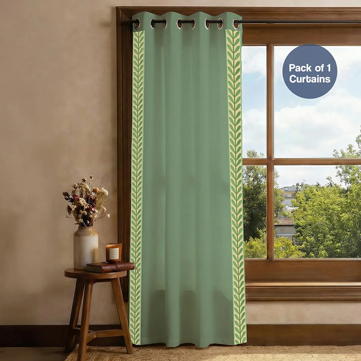 Single green curtain with leafy border hanging across a wooden window