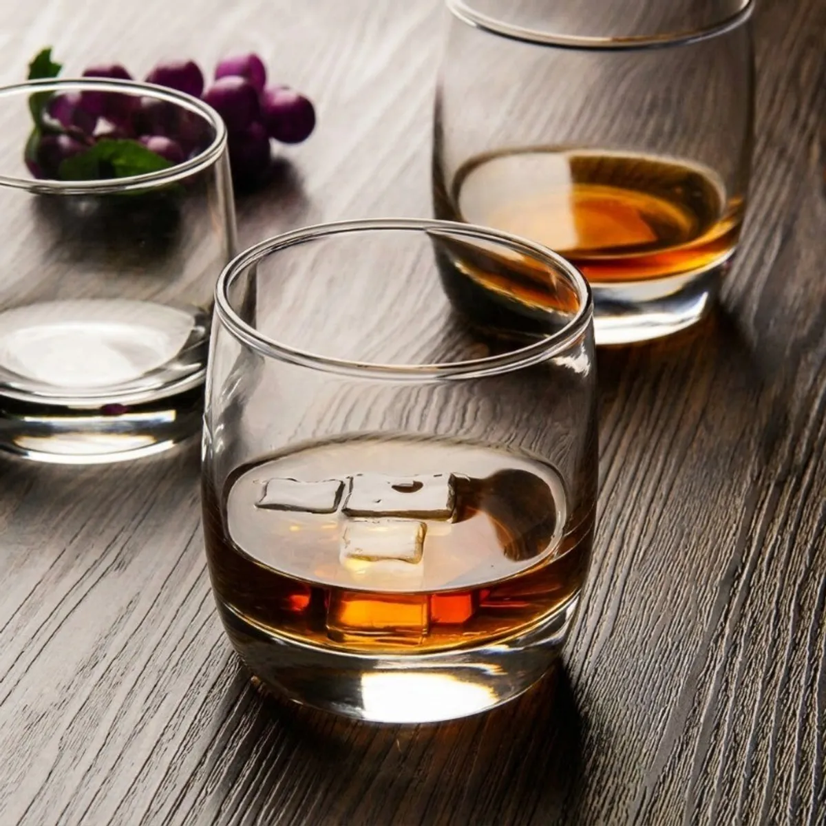 Transparent tumbler holding a dark beverage and ice cubes on a dining table
