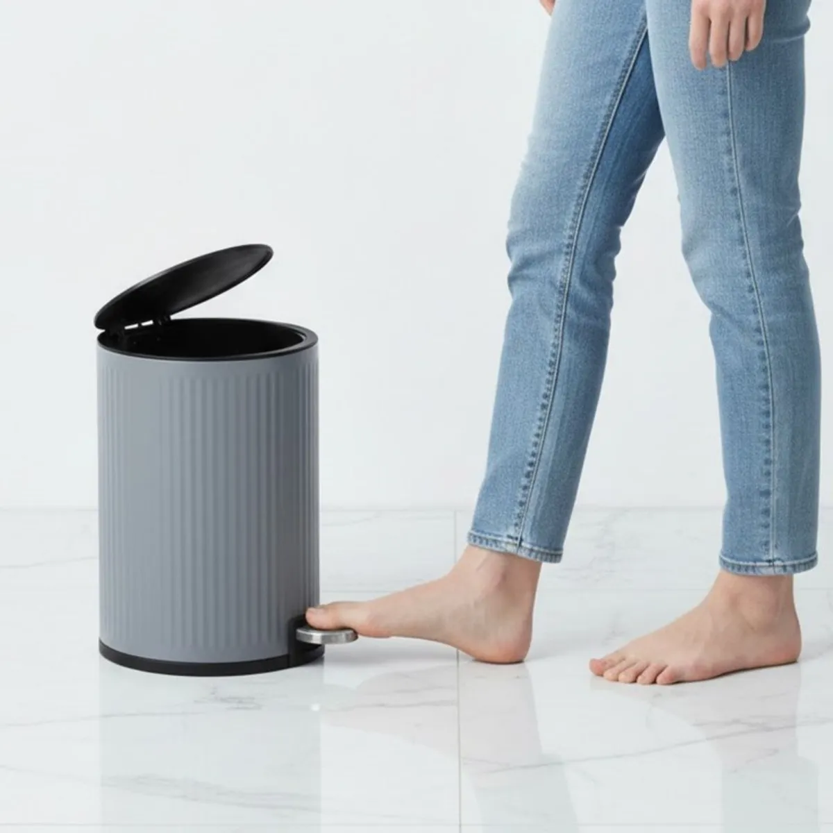 Grey pedal dustbin with lid open beside a person pressing the pedal