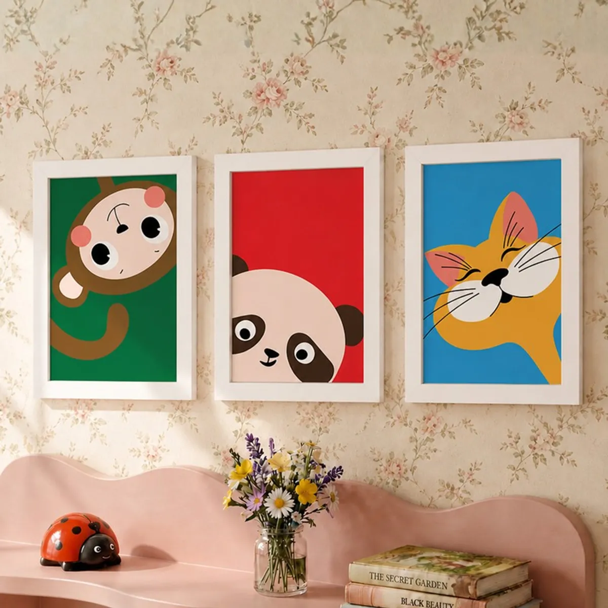 Three white-framed animal prints on a floral wall above a pink shelf