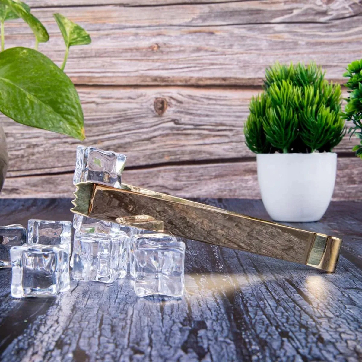 Gold-toned ritual tong shown on a rustic wooden surface with ice cubes