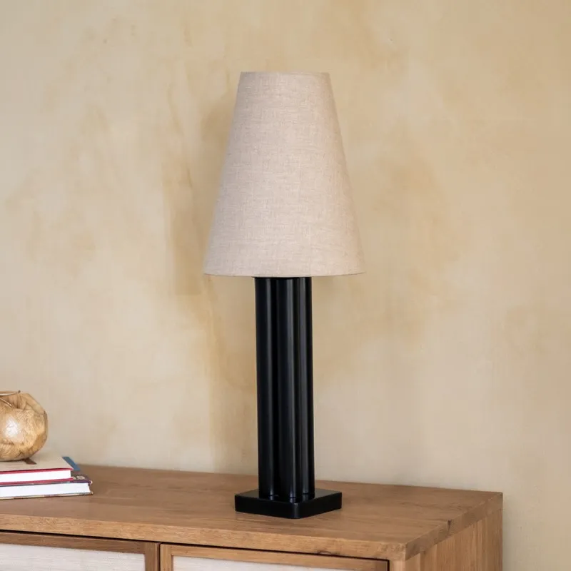 Black table lamp with tapered off-white shade styled on a wooden surface