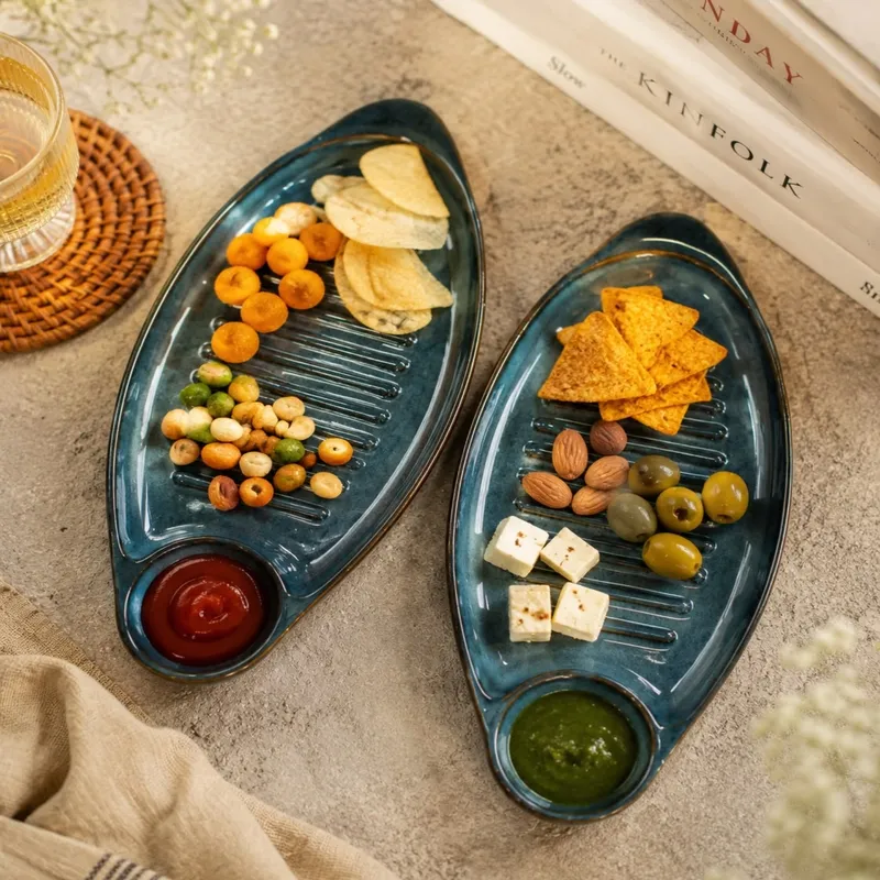 Two blue oval platters arranged with snacks, nuts, olives and dips