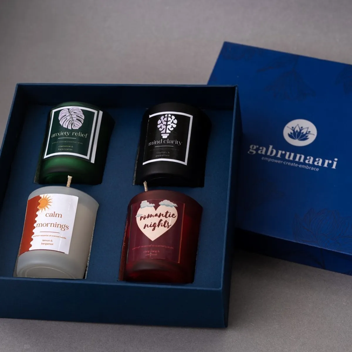 Open blue gift box displaying four colourful jar candles in fitted compartments.