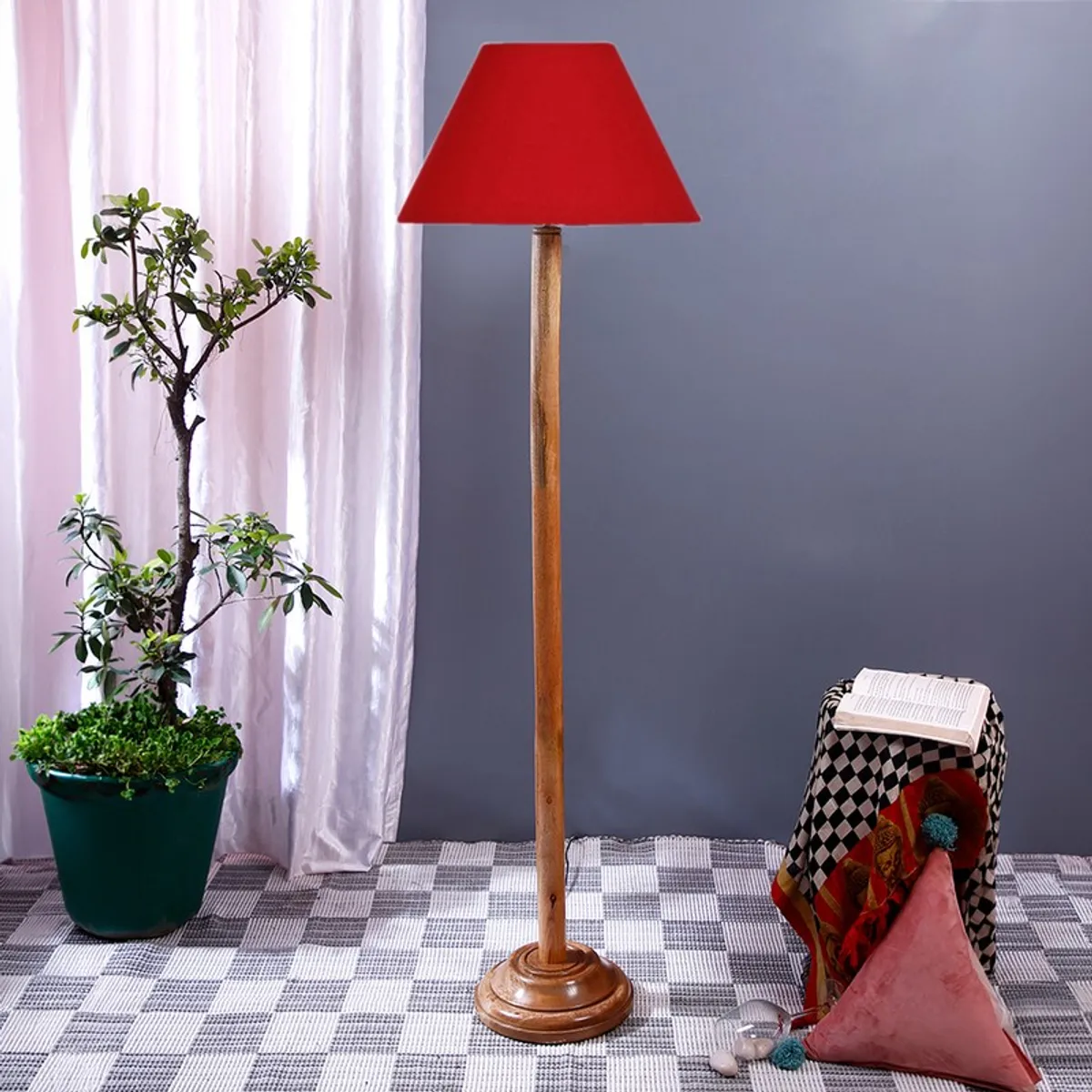 Tall wooden floor lamp with red shade against a grey wall with curtain backdrop