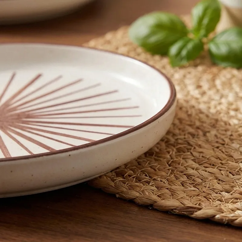 Close-up of white plate with maroon starburst pattern and rim detail