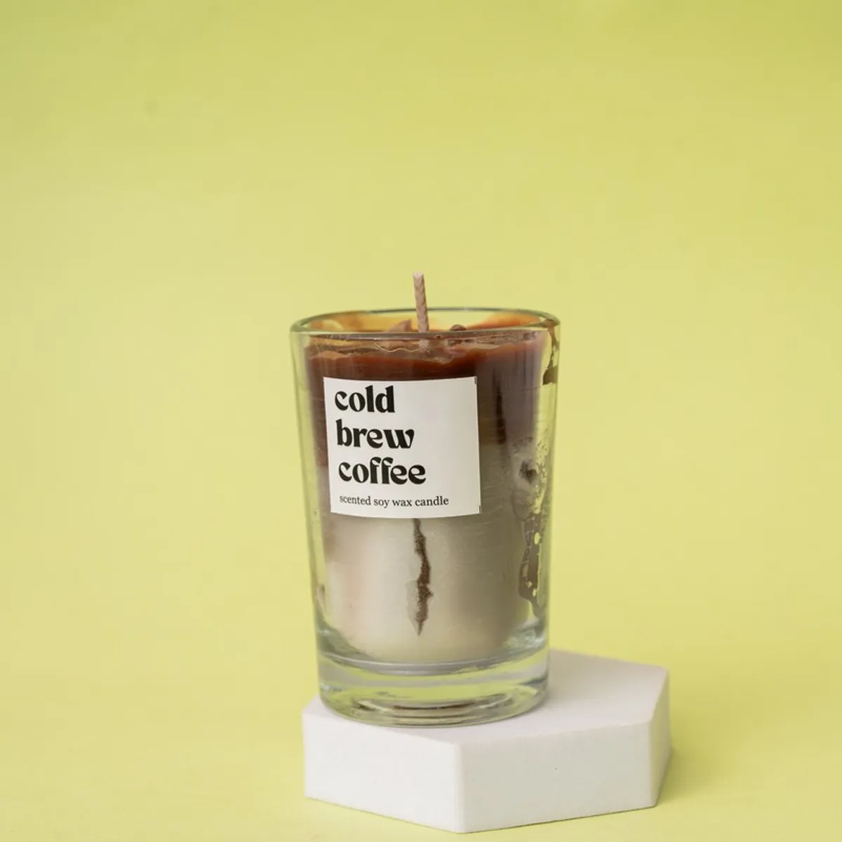 Brown coffee candle in a clear glass jar displayed on a white stand