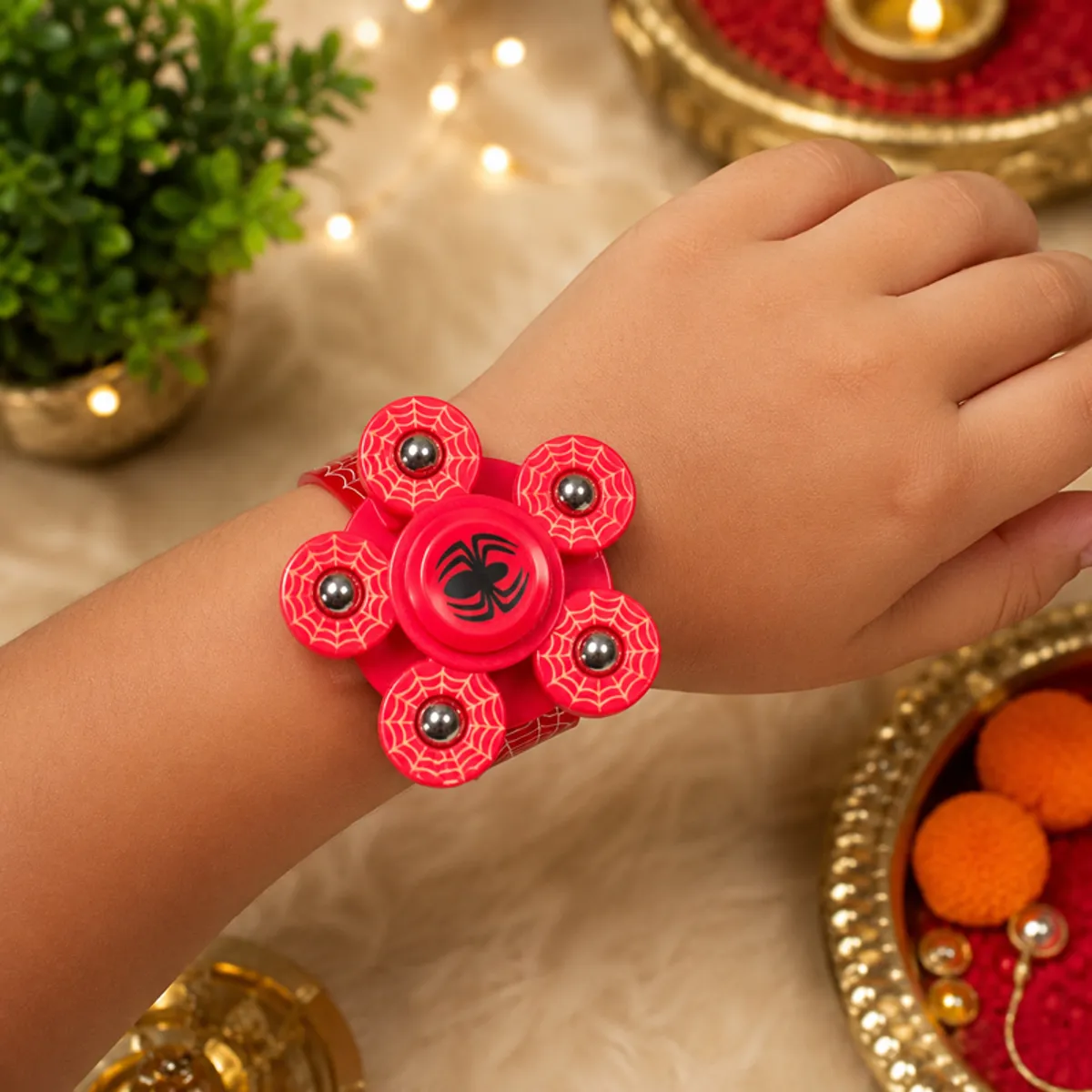 Red spinner rakhi with a spider motif shown on a wrist