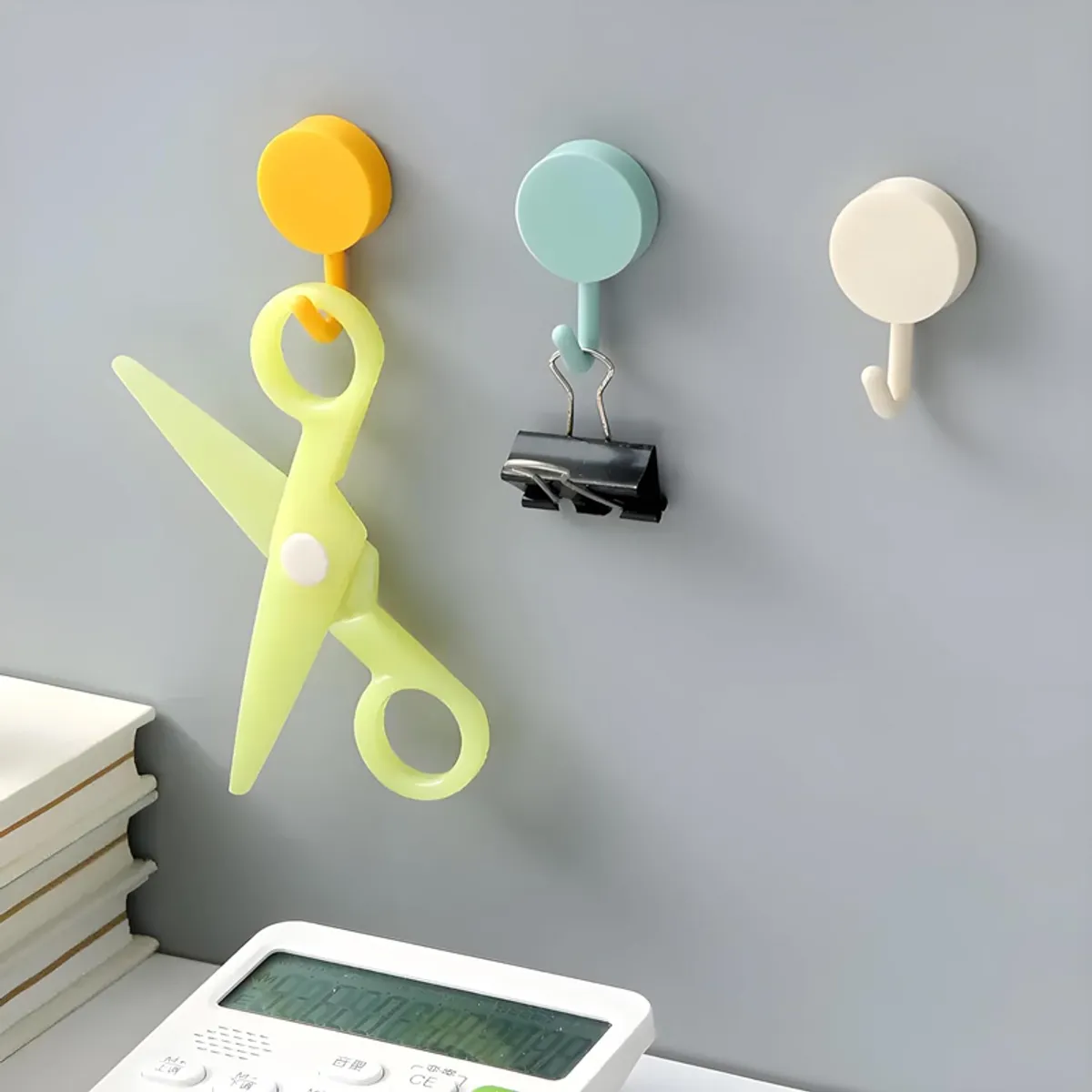 Three pastel round hooks holding scissors, a binder clip and a small object.