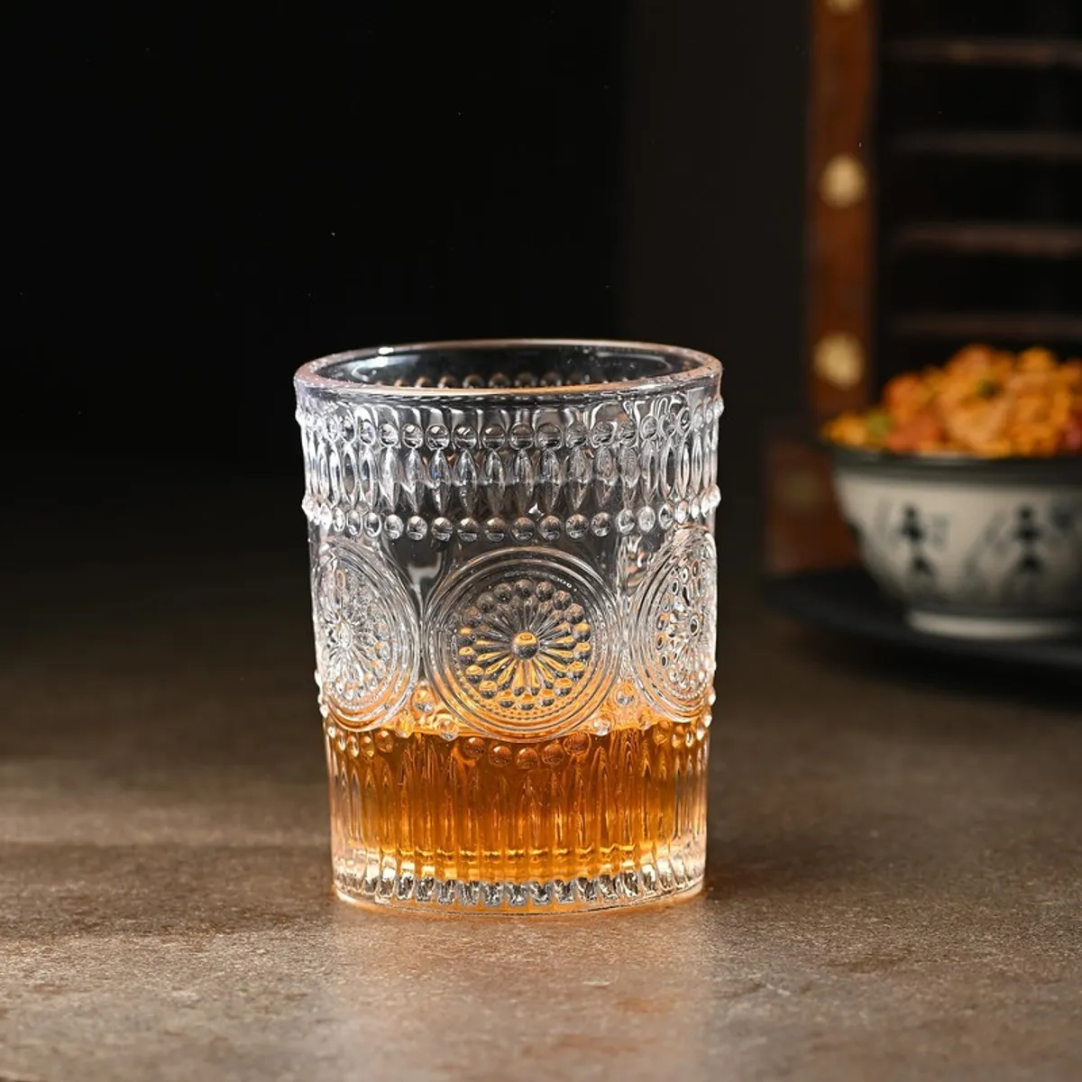 Single clear embossed whiskey glass partly filled with amber drink