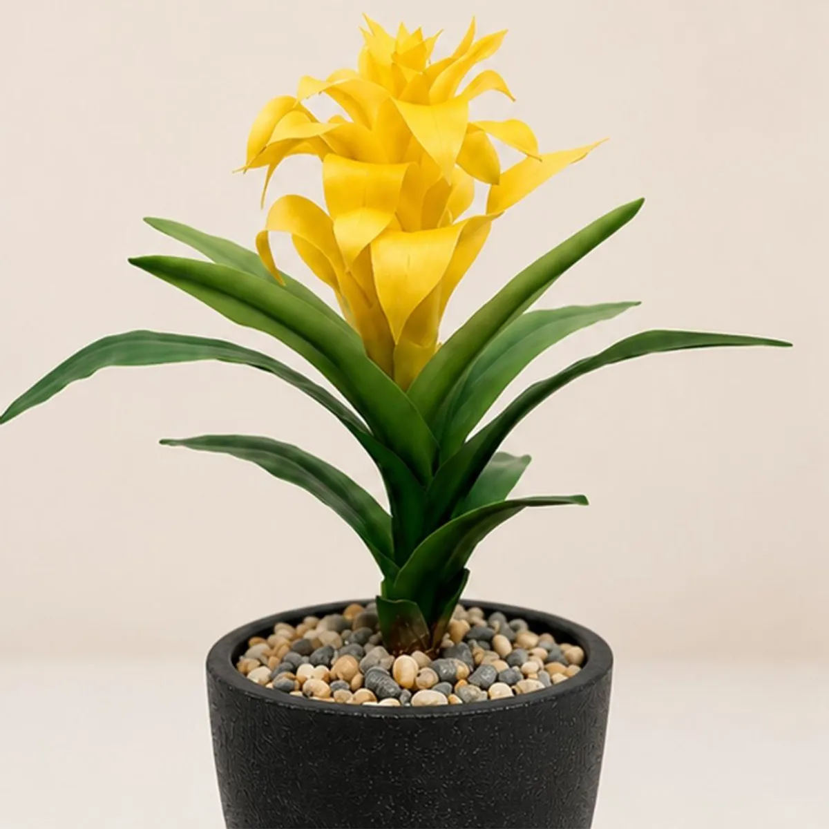 Close-up of yellow artificial bromeliad bloom and green leaves in a black pot