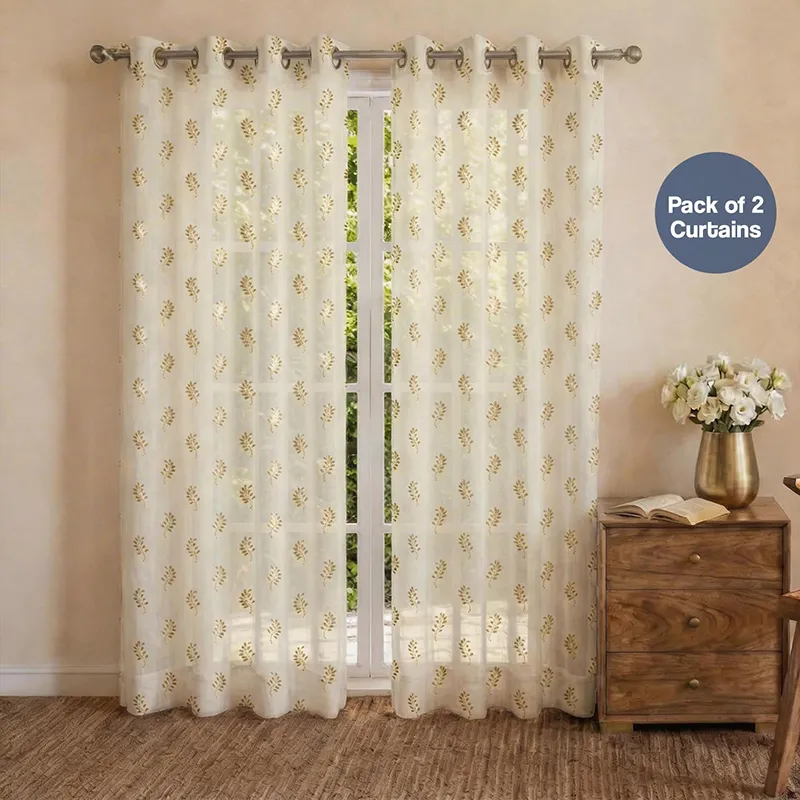 Set of white curtains with gold printed motif hanging on a window with eyelet top