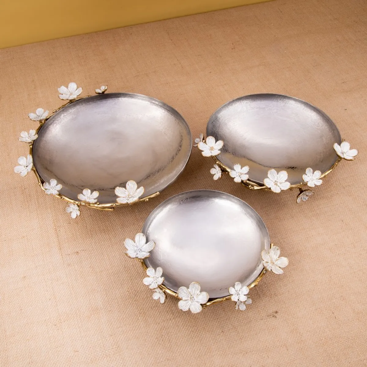 Three silver bowls with gold floral rims arranged on a textured surface