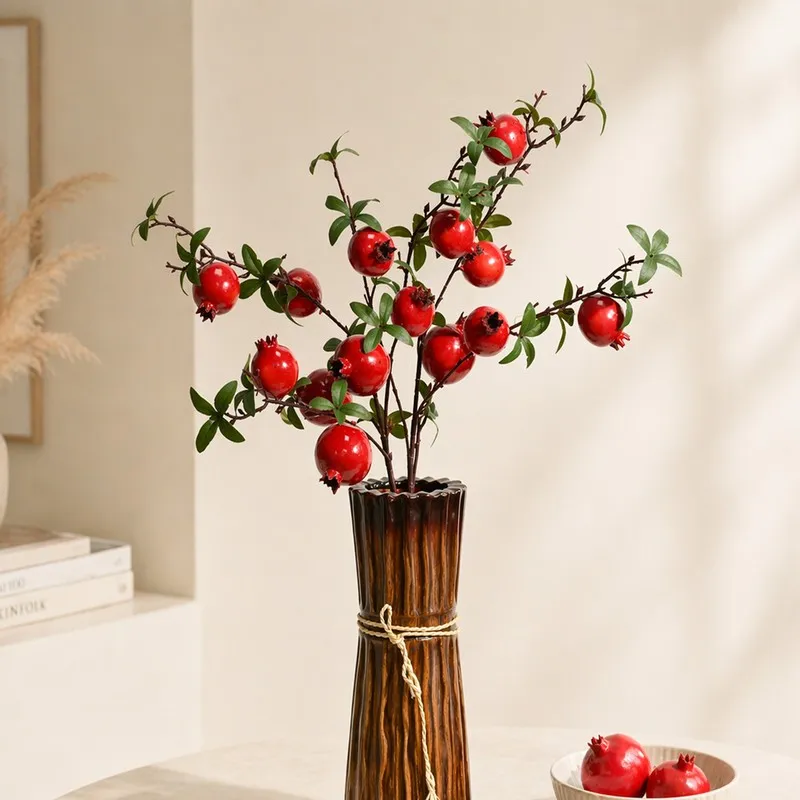 Artificial pomegranate branches arranged in a tall brown vase