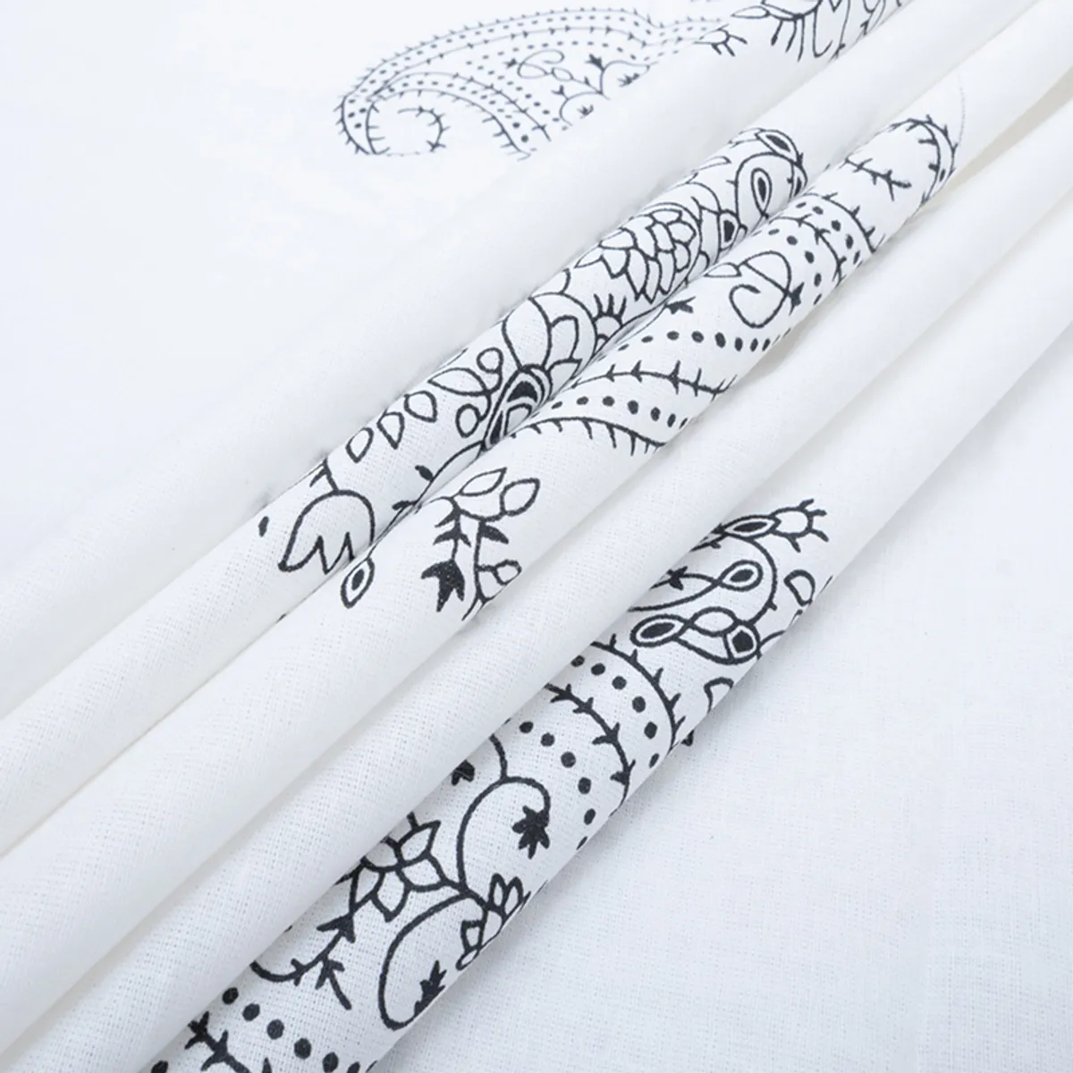 Folded white cotton fabric showing black floral paisley prints