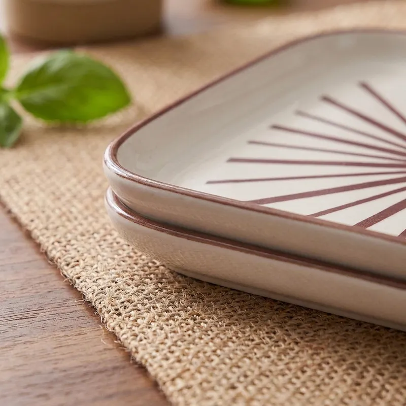 Close-up of square porcelain plate with maroon rim and starburst pattern