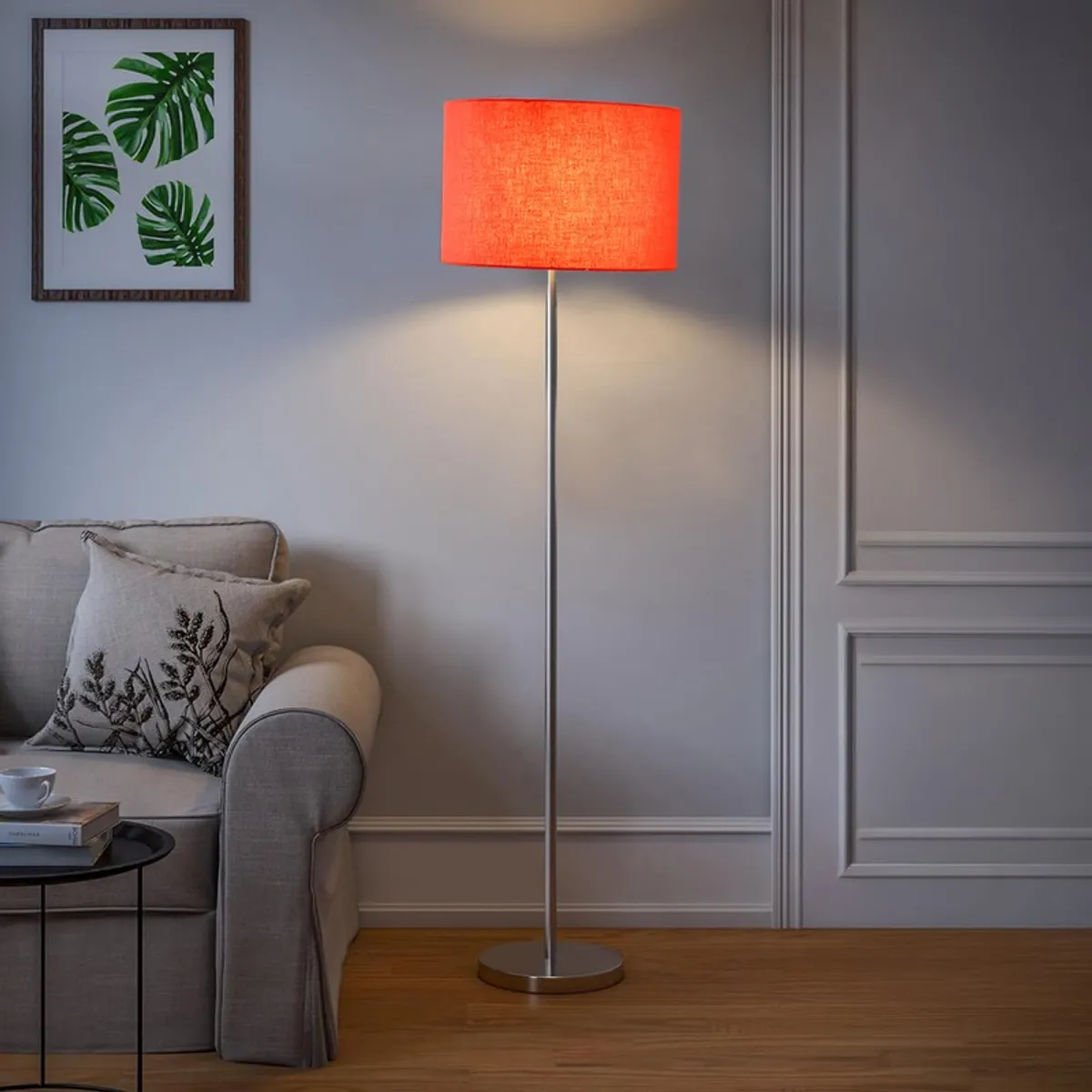 Orange floor lamp with cylindrical shade styled beside a sofa in a neutral room