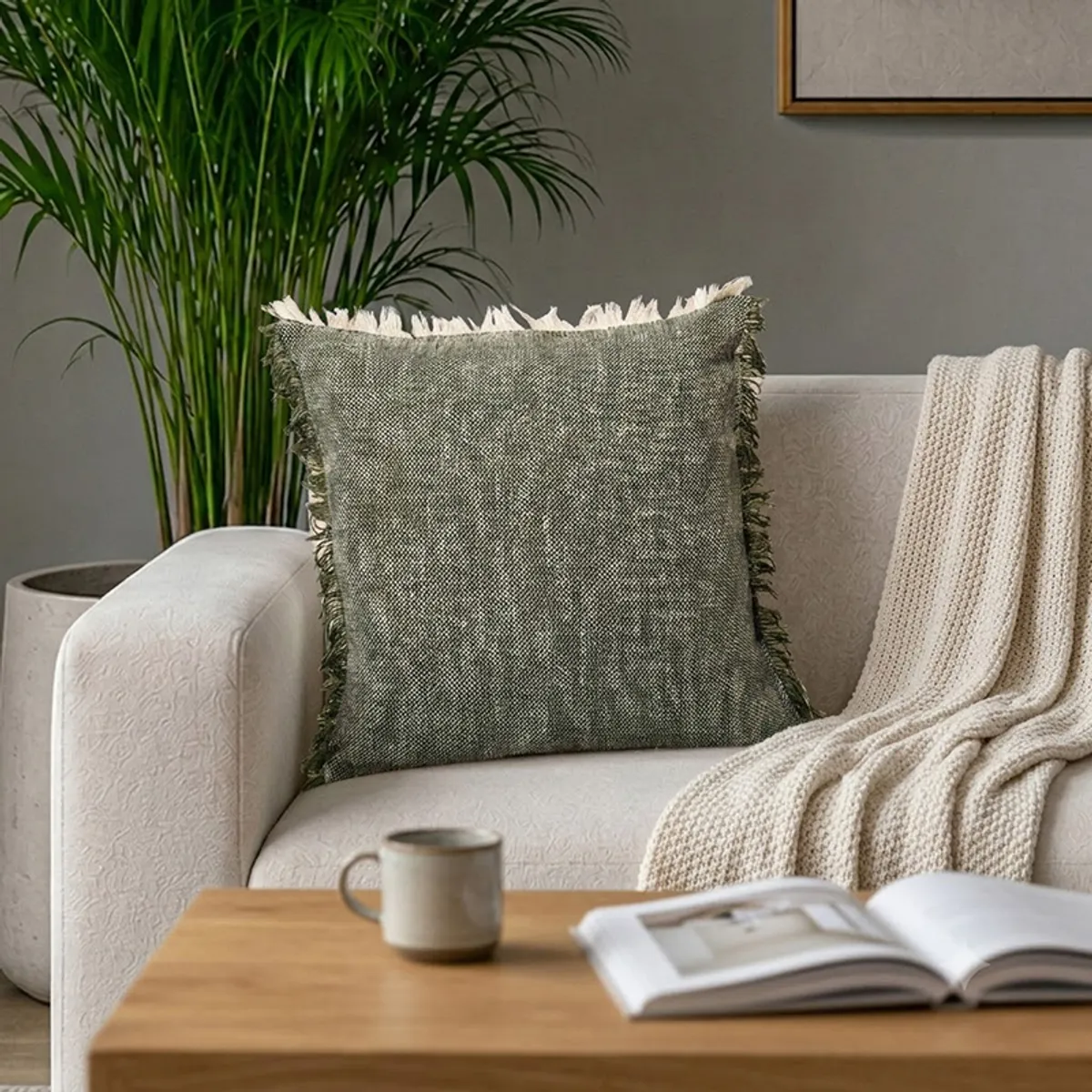Textured fringed cushion cover styled on a sofa with a throw, mug and open book.