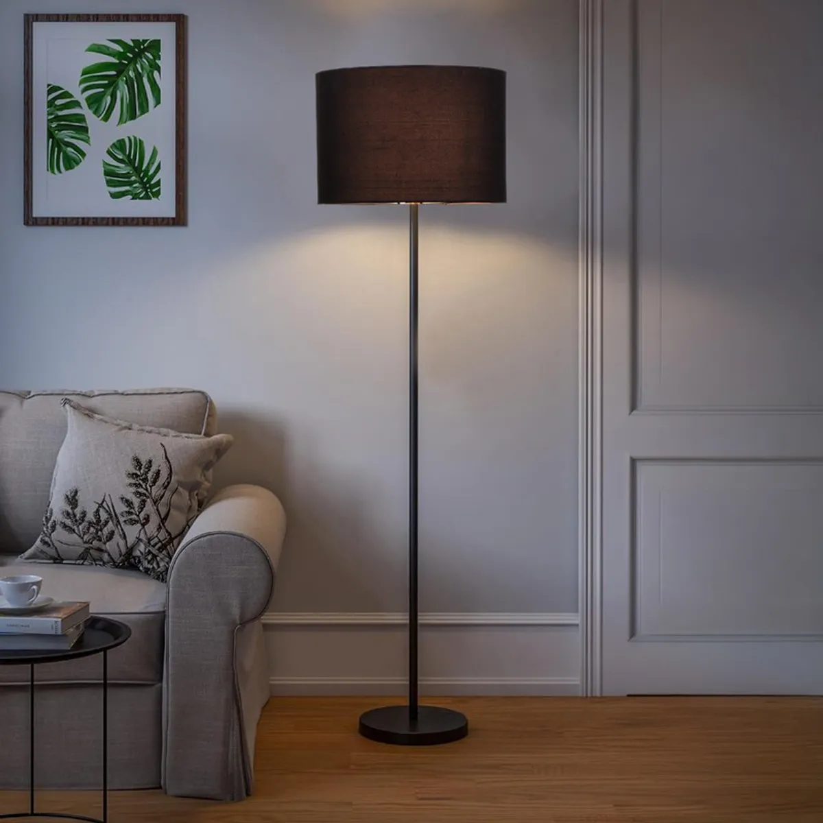 Black floor lamp switched on beside a sofa against a pale wall