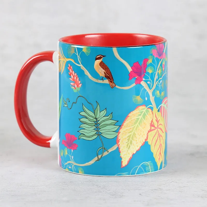 Close-up of a blue ceramic mug with a red handle and tropical bird-and-leaf design