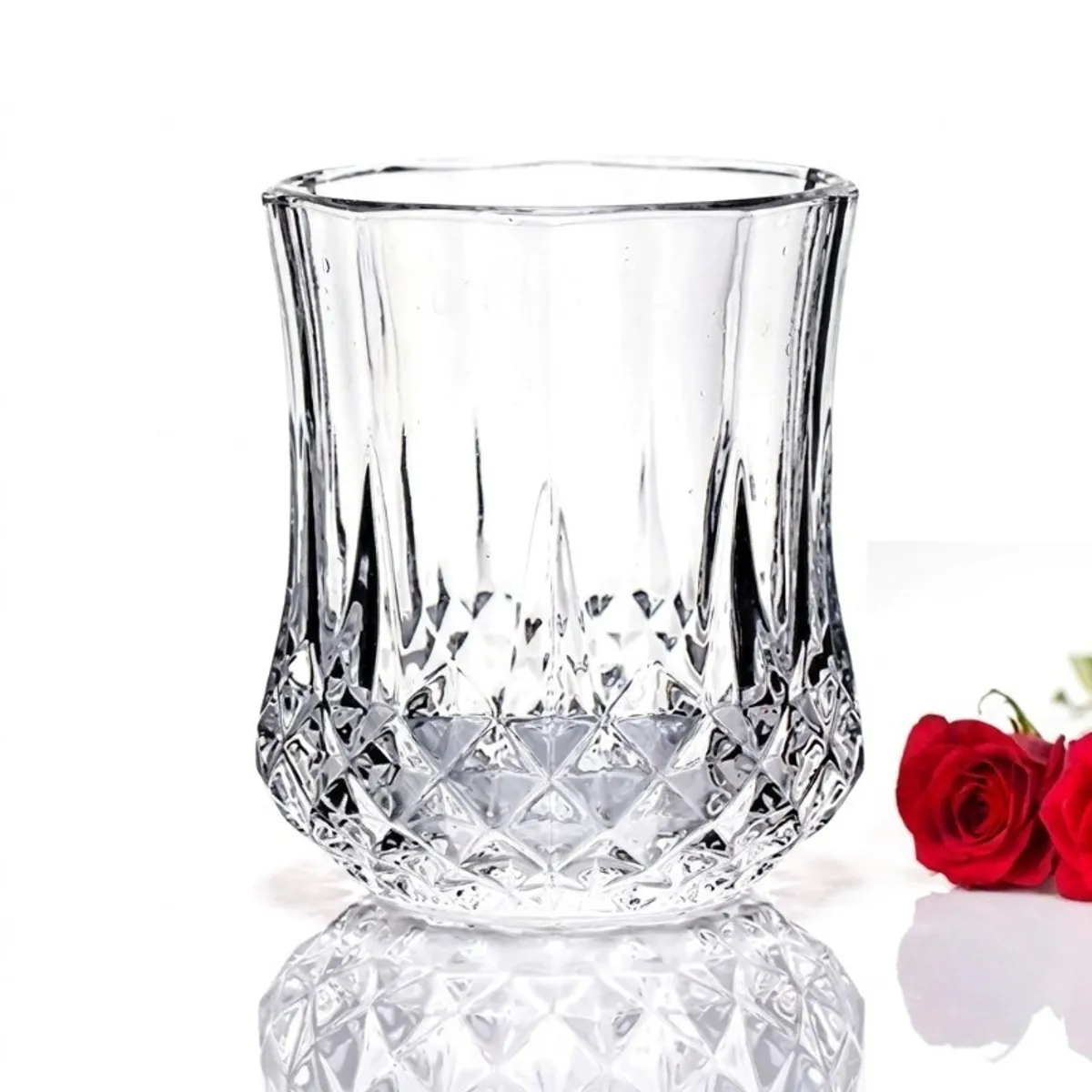 Single clear drinking glass with a faceted textured base beside red roses