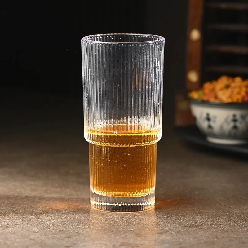 Tall clear ribbed glass filled partly with an amber beverage