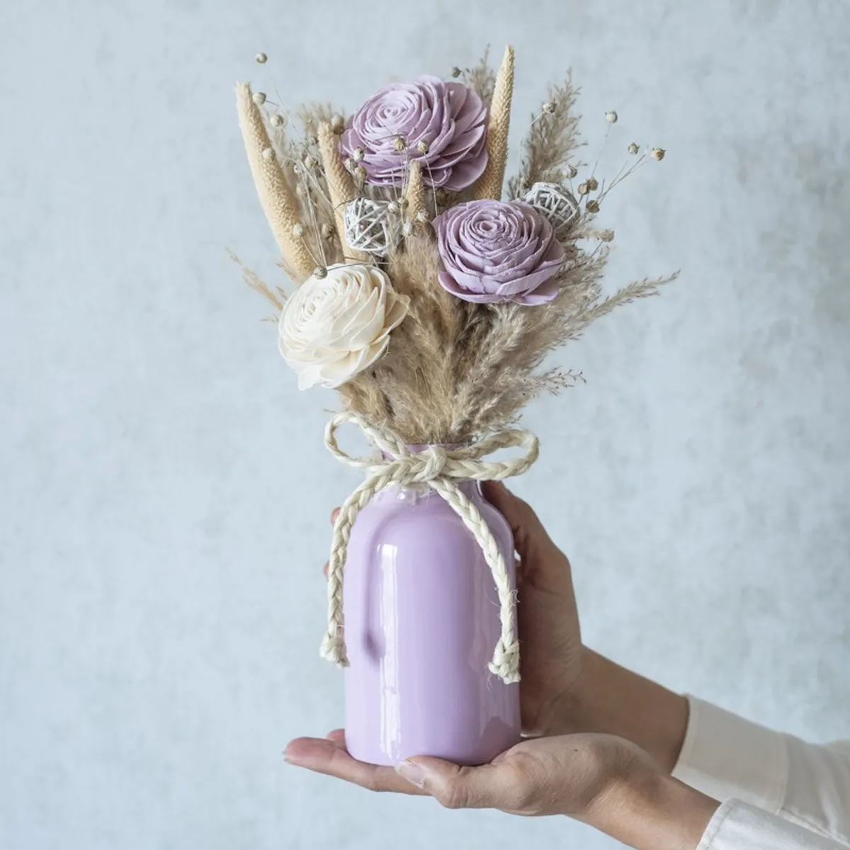 Close view of a beige, white and purple dried flower bunch held in one hand.