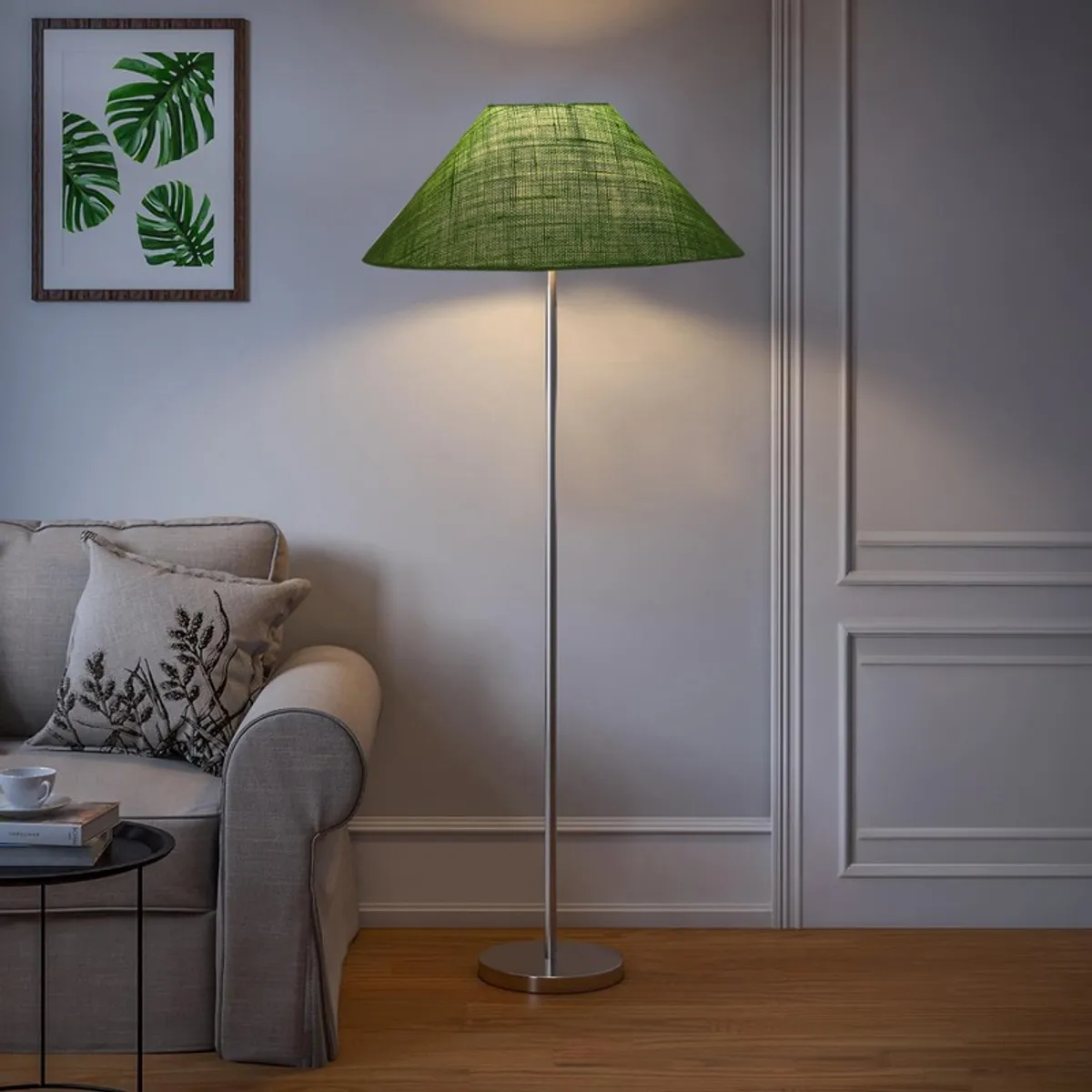 Green floor lamp lit in a living room with sofa and framed leaf artwork
