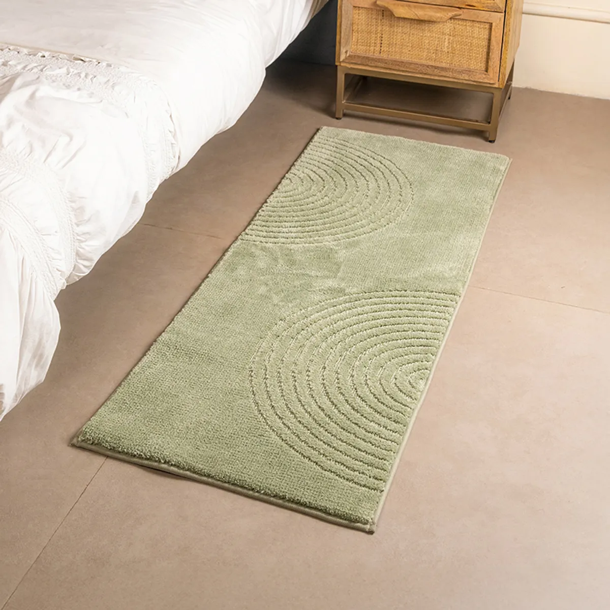 Green runner rug styled alongside a bed, featuring a soft concentric arc design