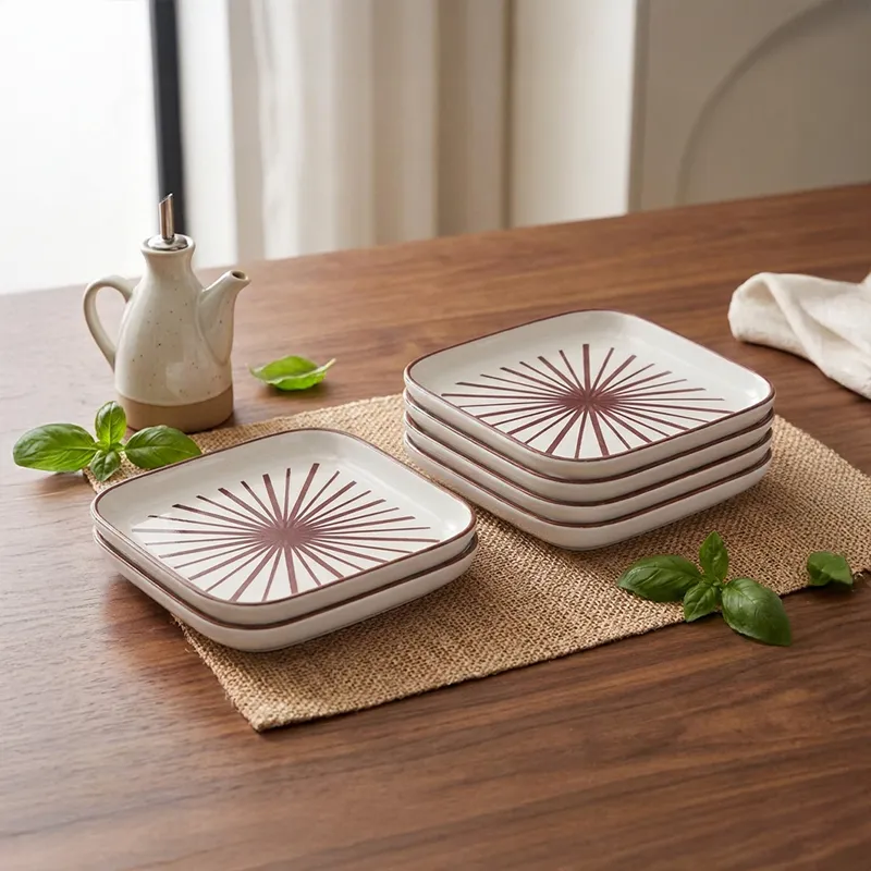Stacked square snack plates with maroon starburst motif on a wooden dining table