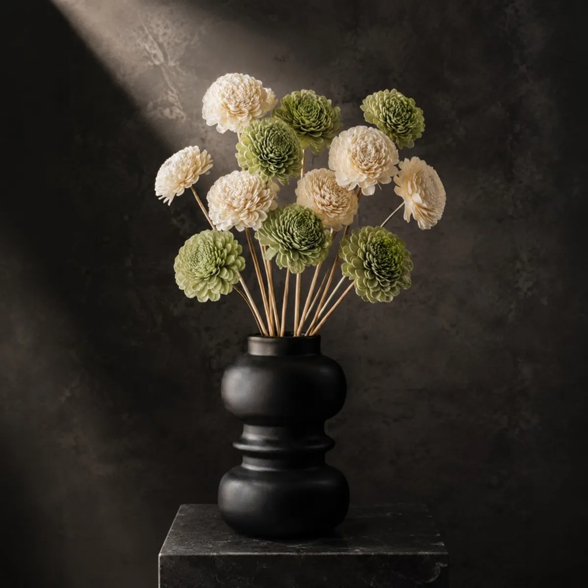 Green and off-white pom-pom flower arrangement in a black sculptural vase