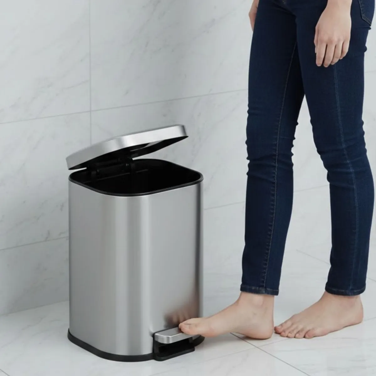 Grey metal pedal dustbin shown open beside a person in a bathroom setting