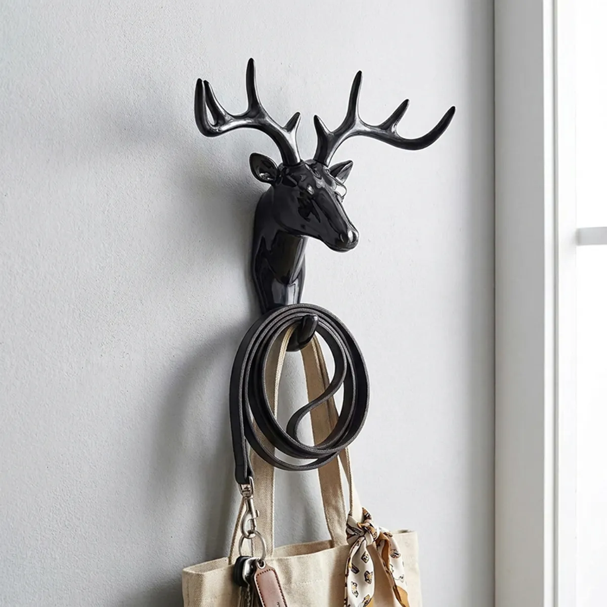 Black deer antler wall hook holding a belt and tote bag