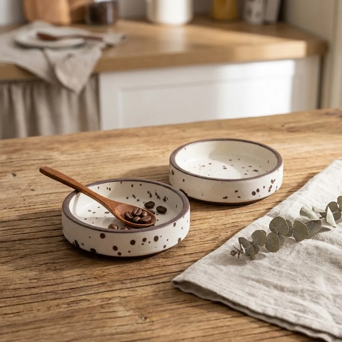 Two speckled white dip bowls on a wooden table, one with a small wooden spoon