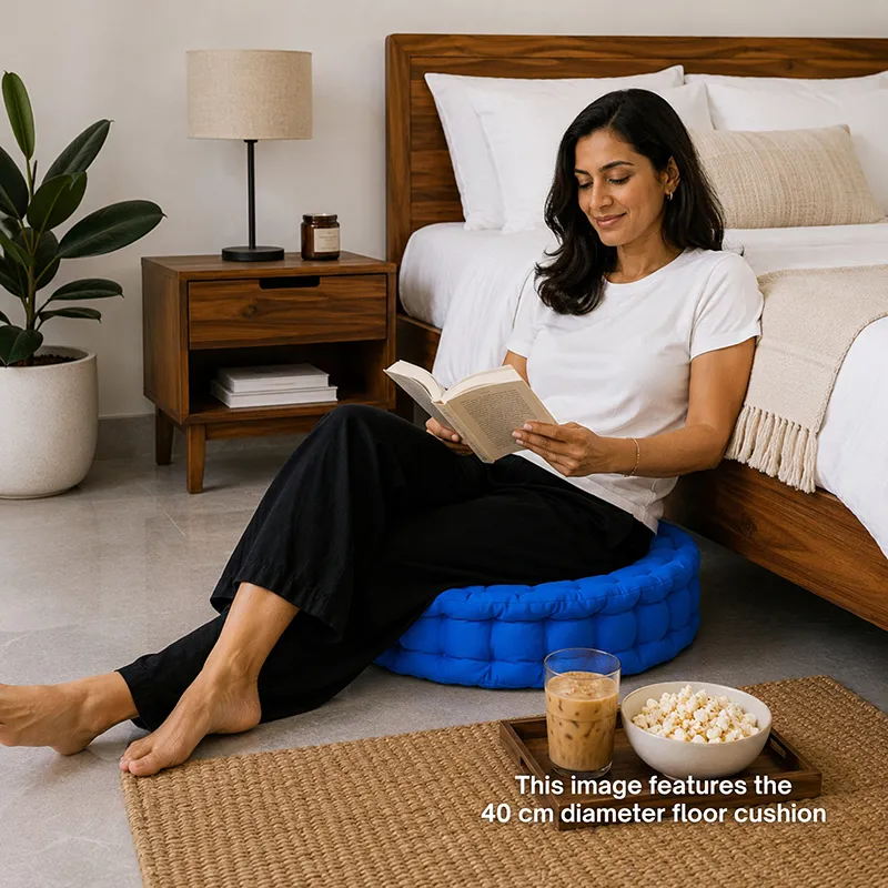 Woman reading while seated on a round blue floor cushion beside a bed