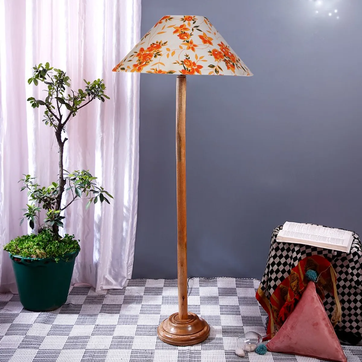 Tall wooden floor lamp with a wide floral shade in a styled indoor setting.