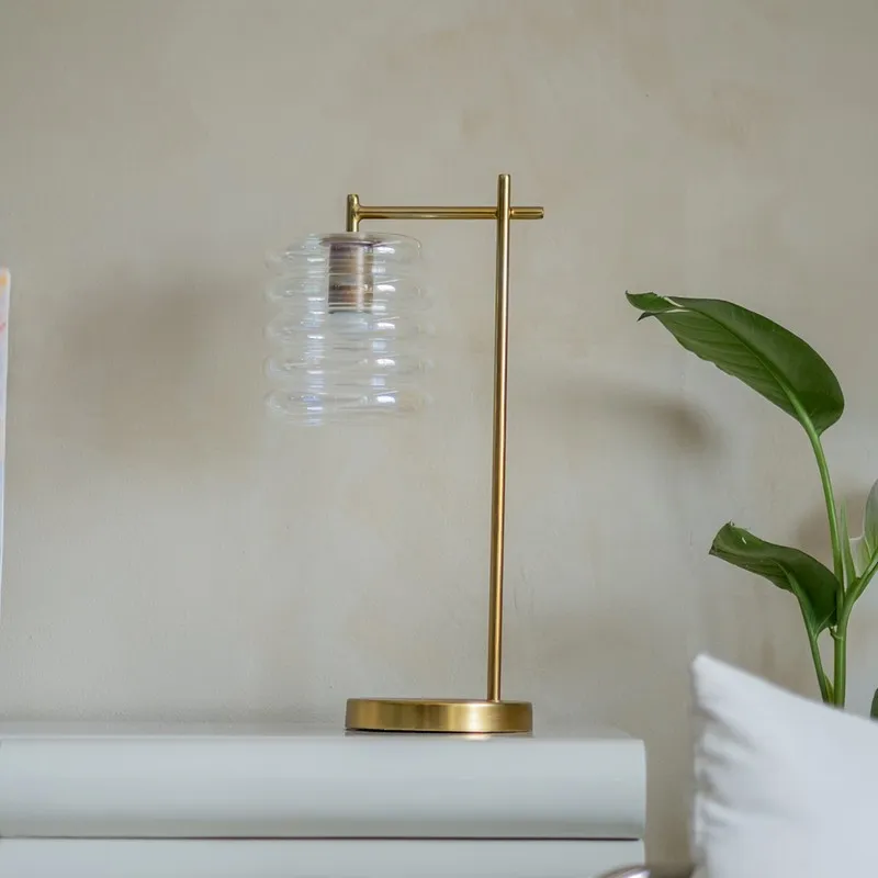 Transparent ribbed glass table lamp with gold-toned stand on a white side table