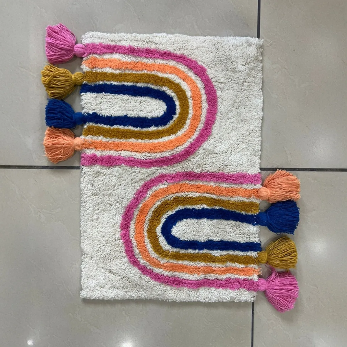 Reverse view of a rectangular colourful arch-patterned bath mat with tassels