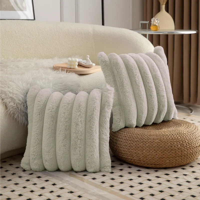 Pale grey plush striped cushion covers arranged on a sofa and woven ottoman.