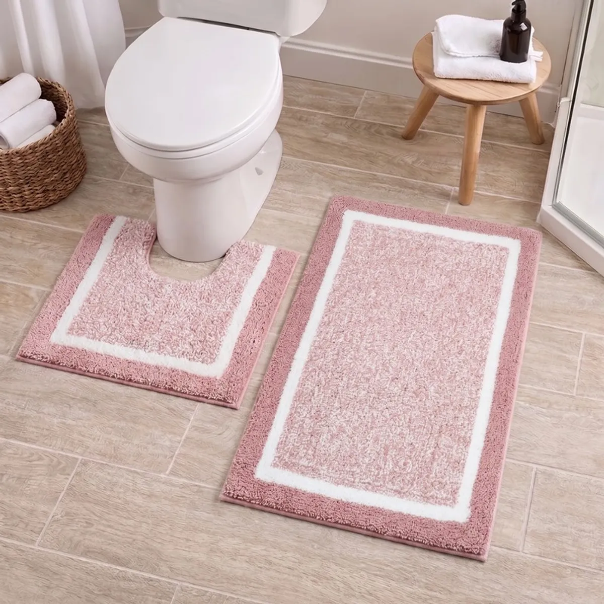 Pink and white bath mats arranged around a toilet on a tiled bathroom floor.